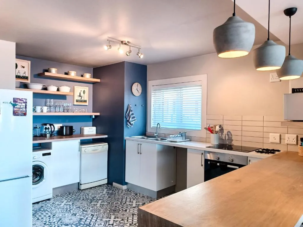 Modern kitchen with blue accent wall, white cabinetry, and pendant lighting