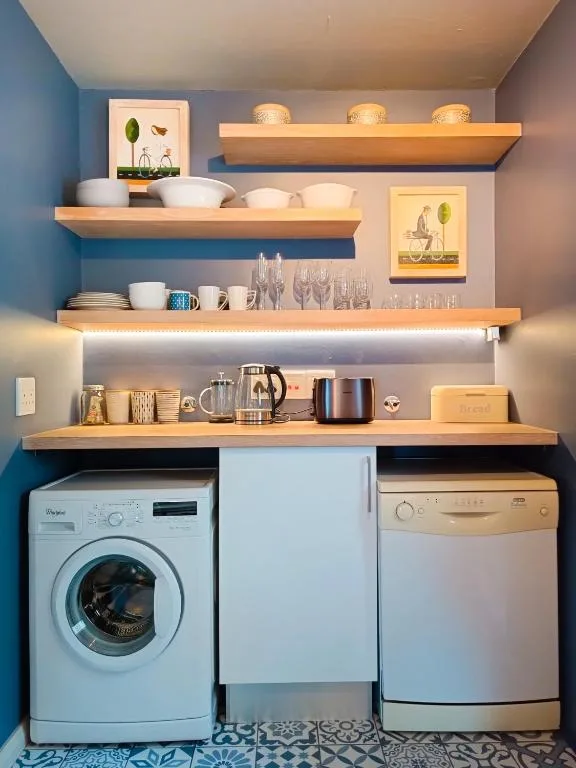 Compact kitchen with wooden shelving, washing machine, and dishwasher