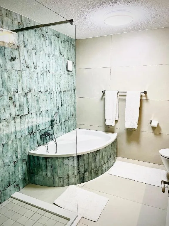 Modern bathroom with curved corner bathtub, green tile shower enclosure, white tiles