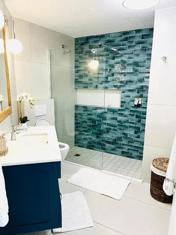 Modern bathroom with teal tile shower wall, white vanity, and glass enclosure