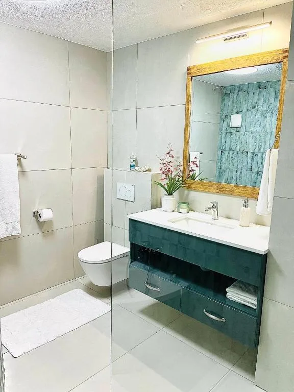 Modern bathroom with green vanity, walk-in shower, and wooden-framed mirror