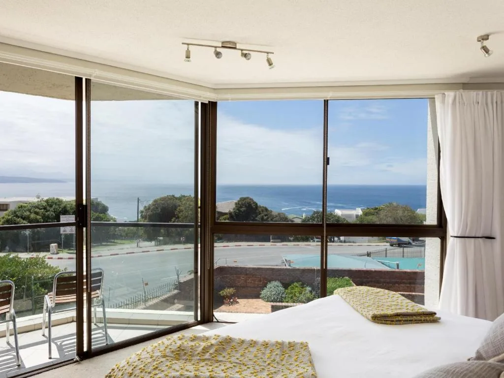 Bedroom with ocean view through floor-to-ceiling windows and pool below
