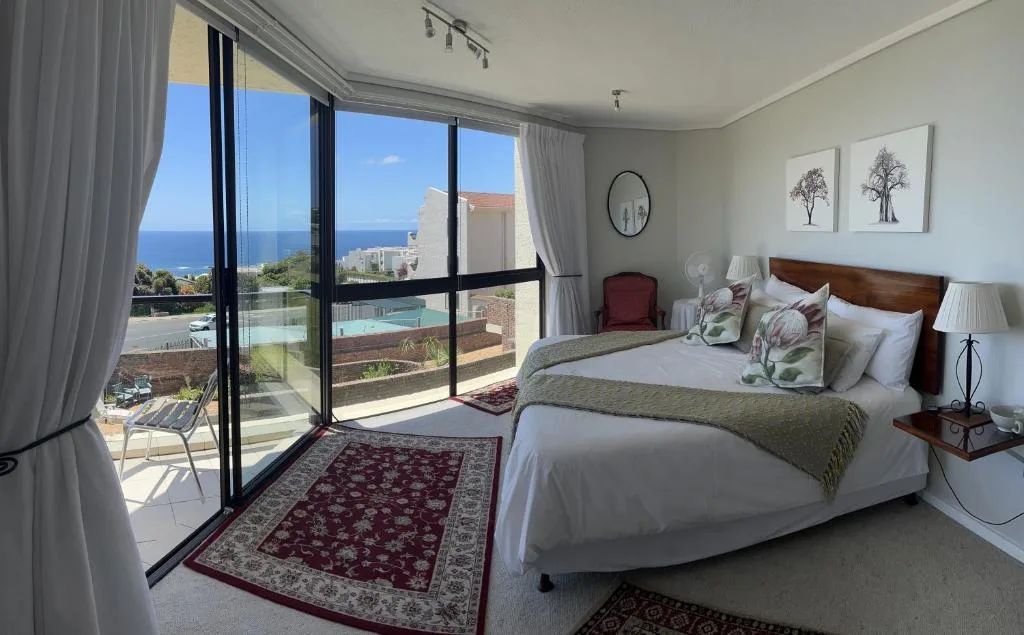 Bright bedroom with ocean view through glass doors and pool visible below