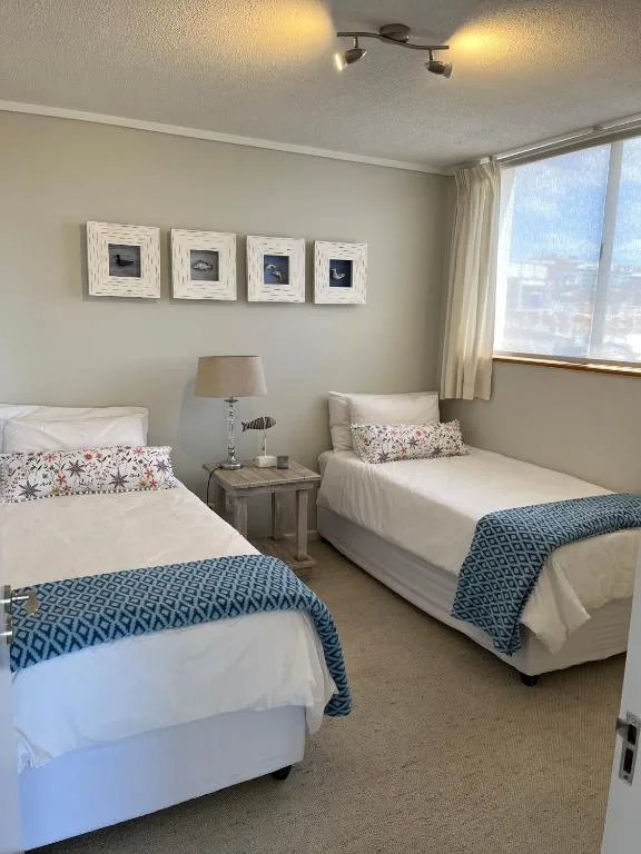 Twin bedroom with blue throws, framed coastal art, and large windows