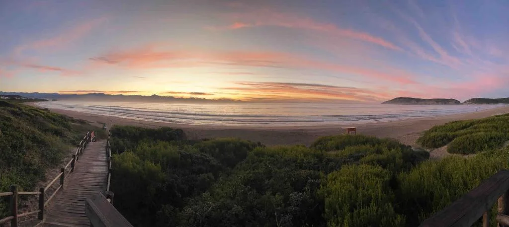 Panoramic beach sunset with golden sky and distant mountains