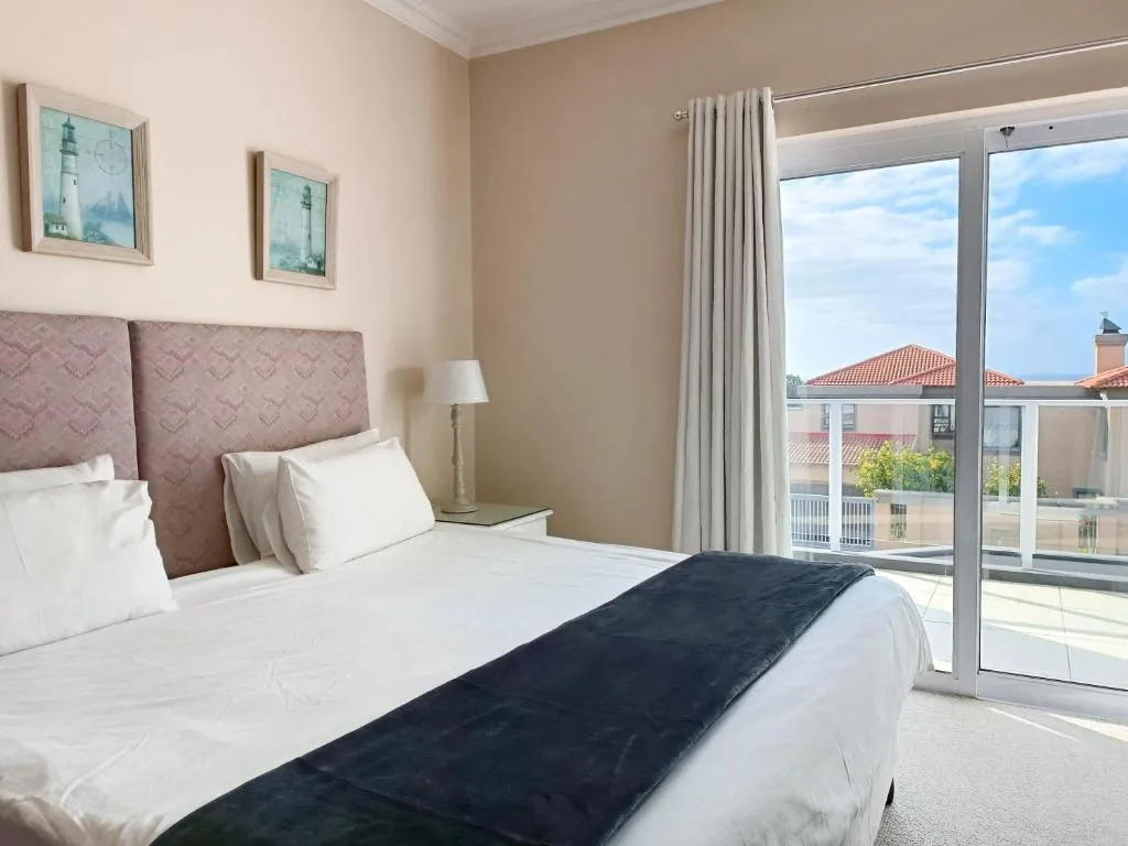 Bright bedroom with queen bed, mauve headboard, and sliding glass doors opening to ocean view.