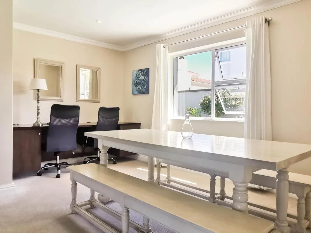 Bright lounge with dining table, office chairs, and large windows overlooking the garden