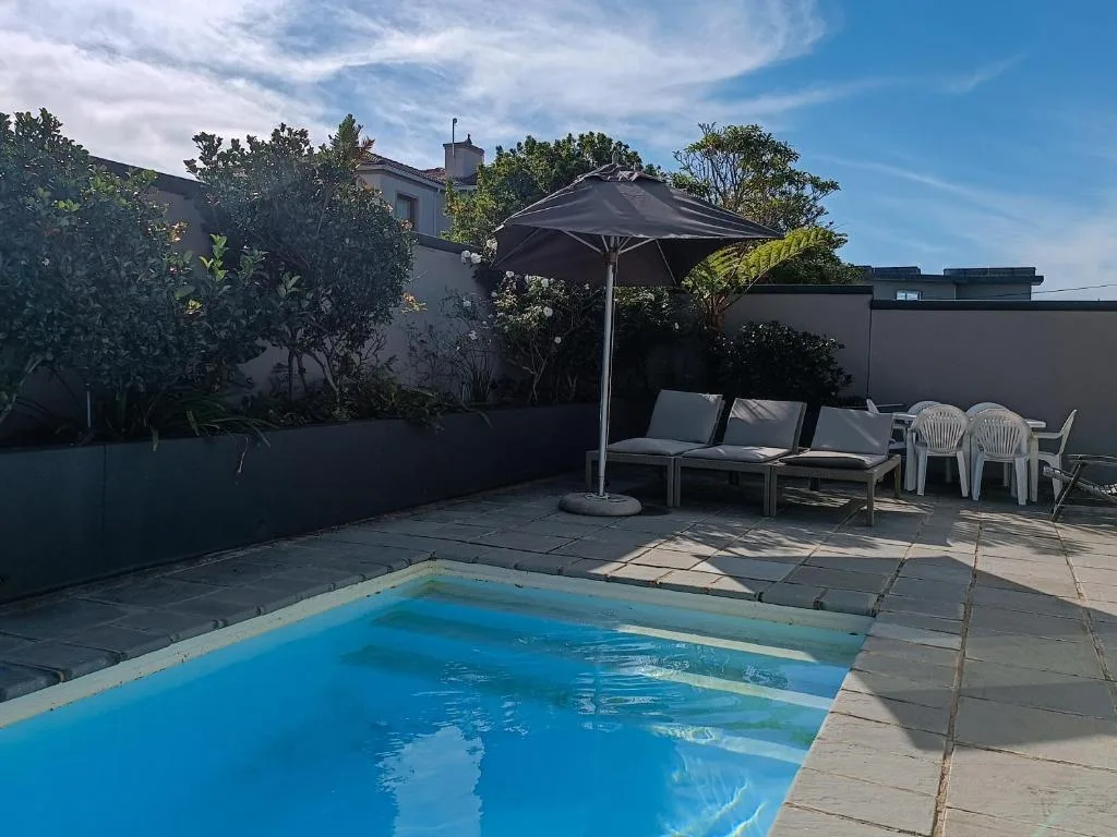 Swimming pool with sun umbrella and lounge seating on paved deck