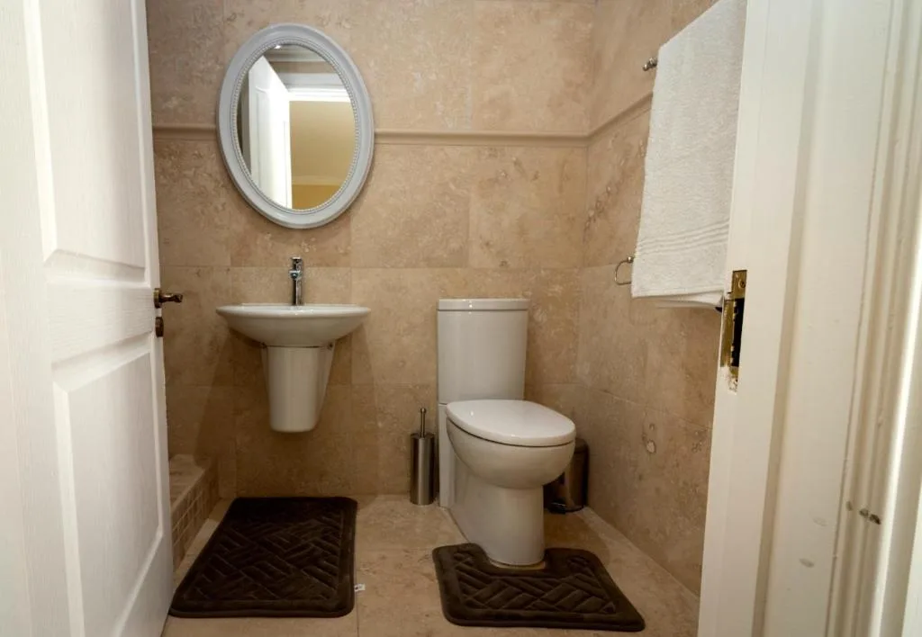 Bathroom with toilet, pedestal sink, oval mirror, and beige tile walls