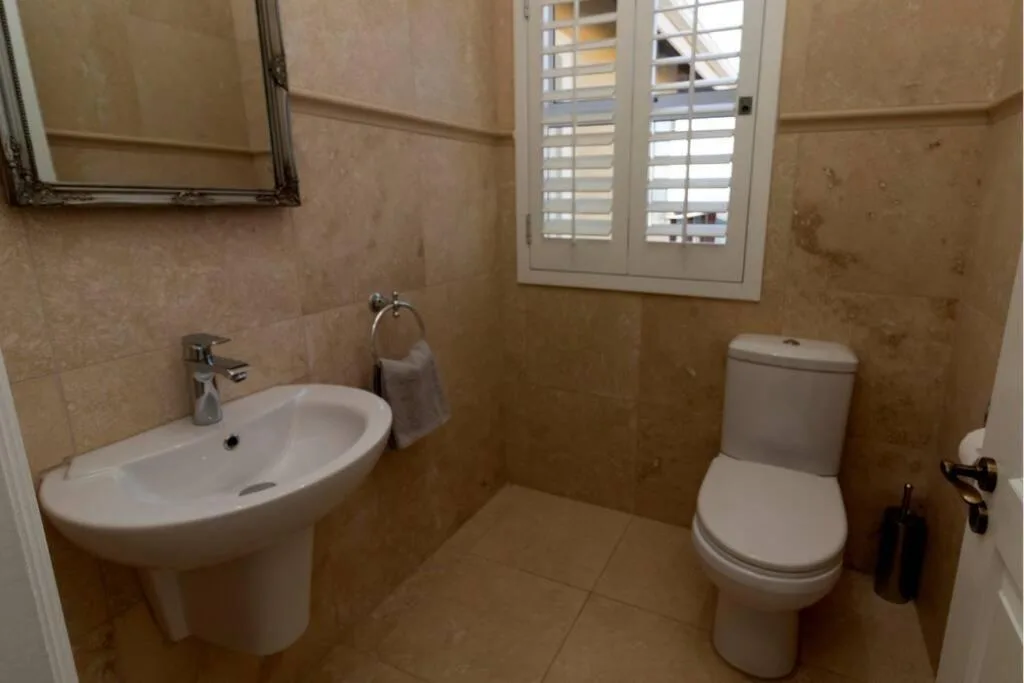 Bathroom with vanity sink, toilet, and window with shutters