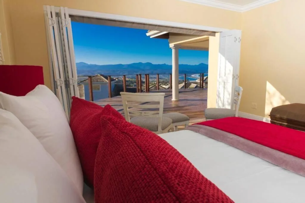 Bright bedroom with red bedding overlooking mountain and coastal views through open doors