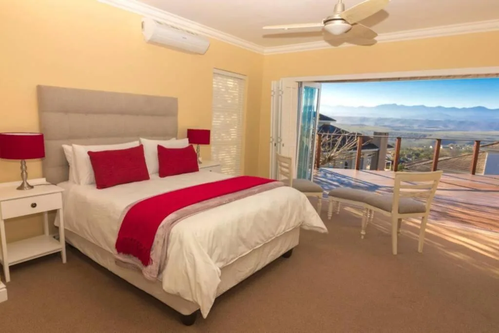 Spacious bedroom with red bedding, mountain view through glass doors