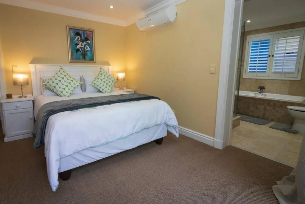 Bright yellow bedroom with white bed, green cushions, and ensuite bathroom