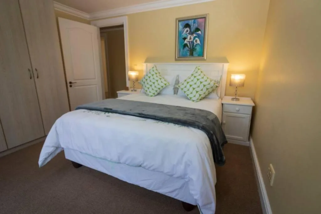 Bright bedroom with queen bed, green cushions, and warm lighting