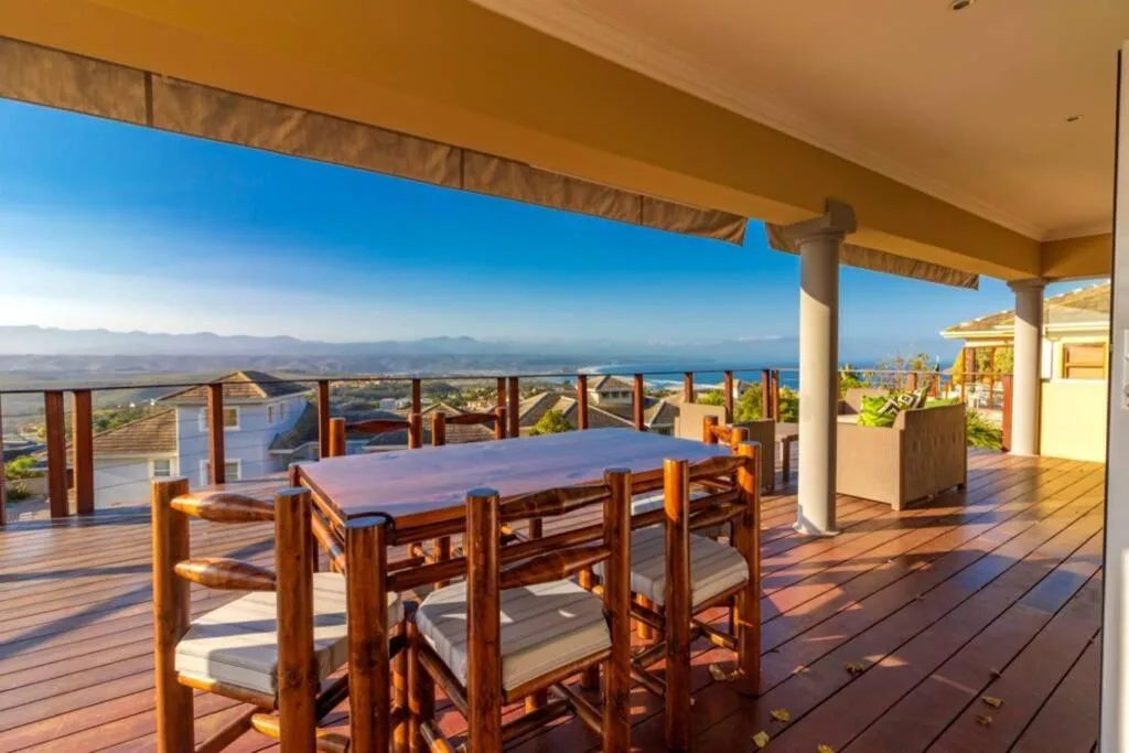 Expansive wooden deck with dining table overlooking coastal mountains and sea