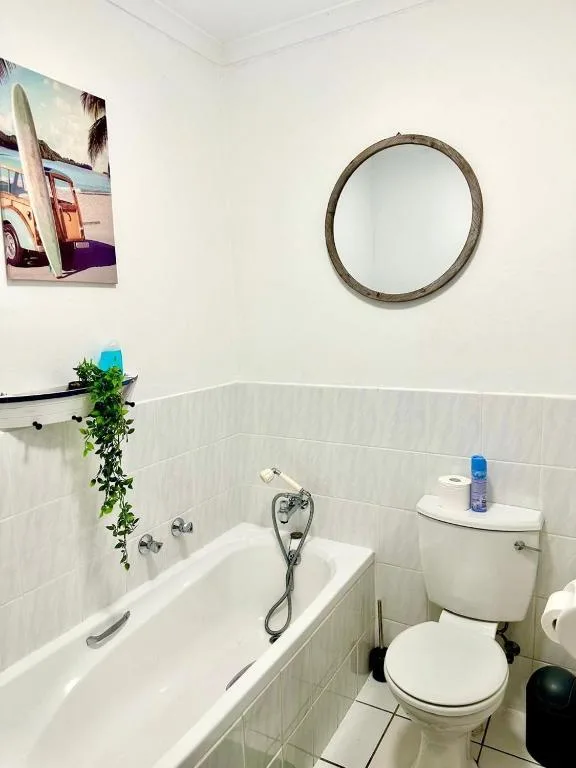 Clean white bathroom with bathtub, toilet, circular mirror, and potted plants