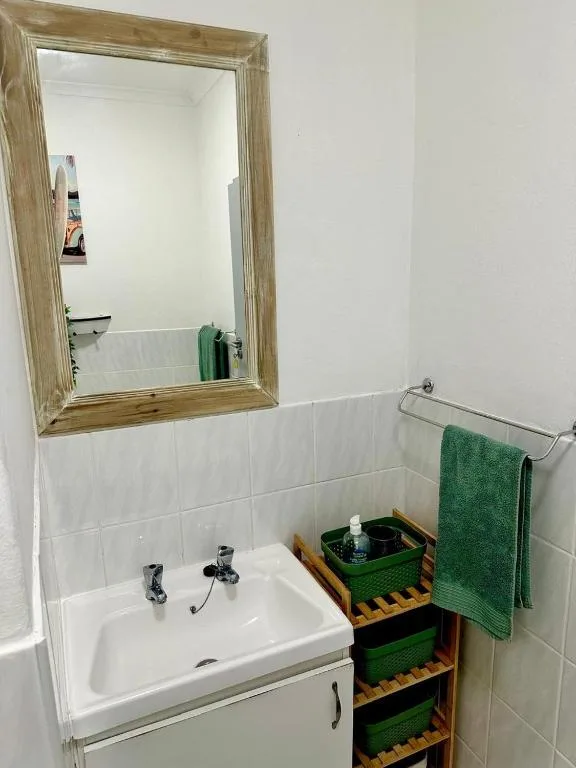 Clean bathroom with white sink, wooden-framed mirror, and green towels