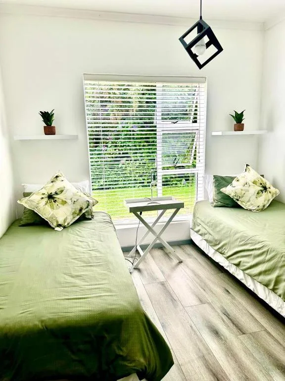 Twin bedroom with green bedding, potted plants, and garden views through shutters