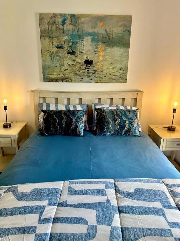 Coastal-themed bedroom with blue bedding and impressionist artwork above headboard