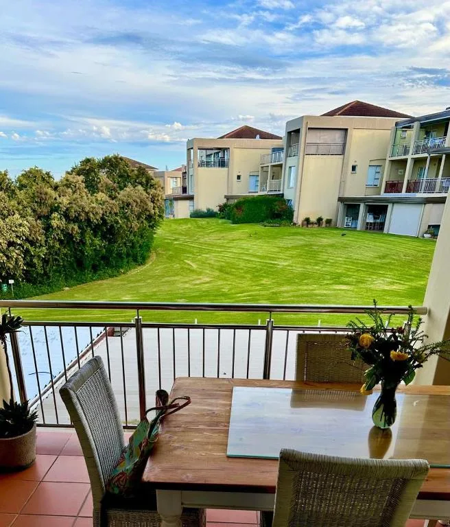 Spacious balcony with dining table overlooking manicured gardens and apartments
