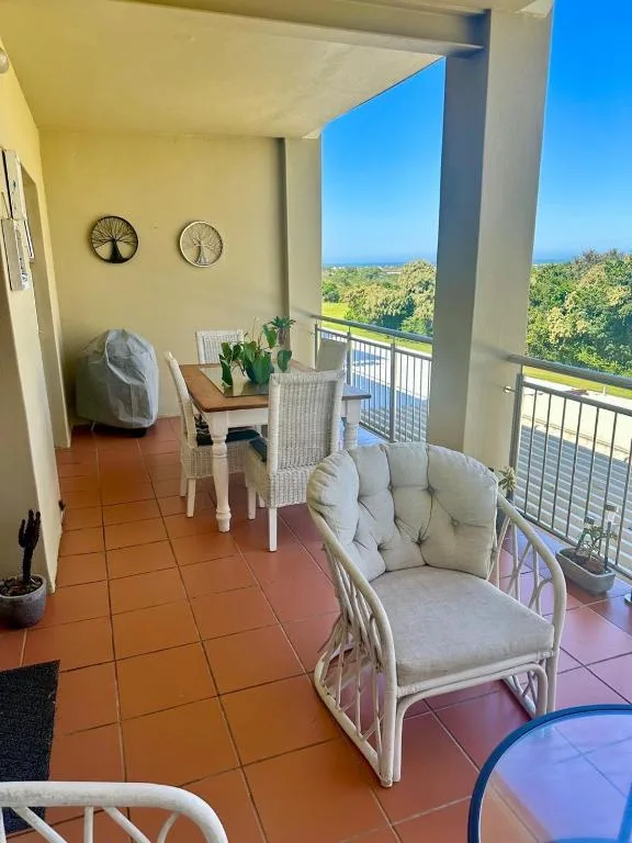 Covered balcony with seating, potted plants, and green hillside views