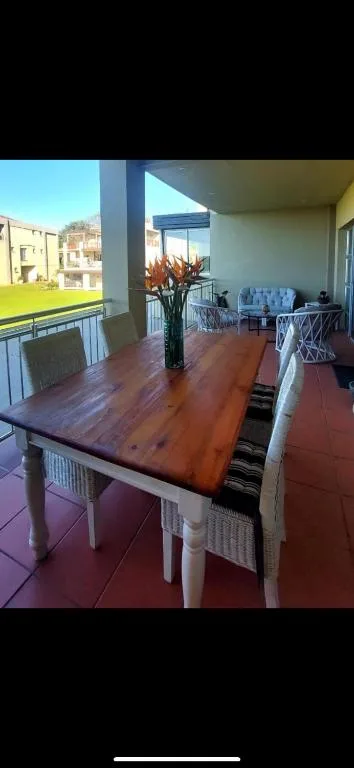 Wooden dining table with white chairs on covered deck overlooking garden