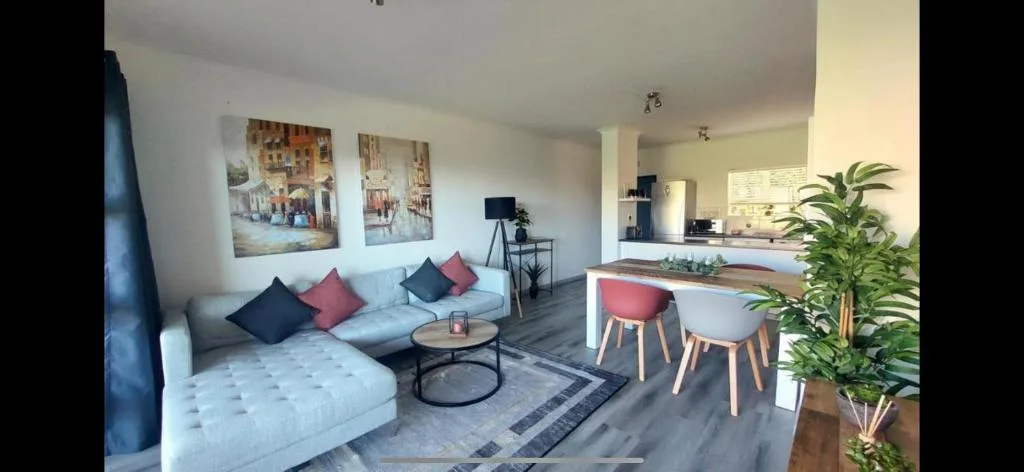 Modern lounge with light blue sofa, colorful cushions, and open-plan kitchen view