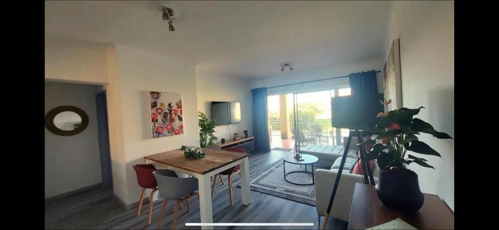 Bright open-plan lounge with sofa, dining table, and glass doors to deck