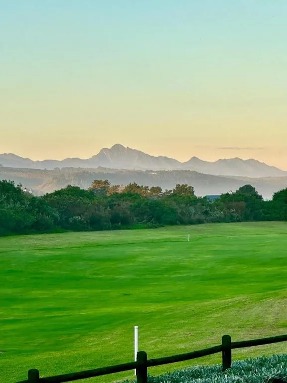 Mountain range at sunrise beyond lush green meadow and fence