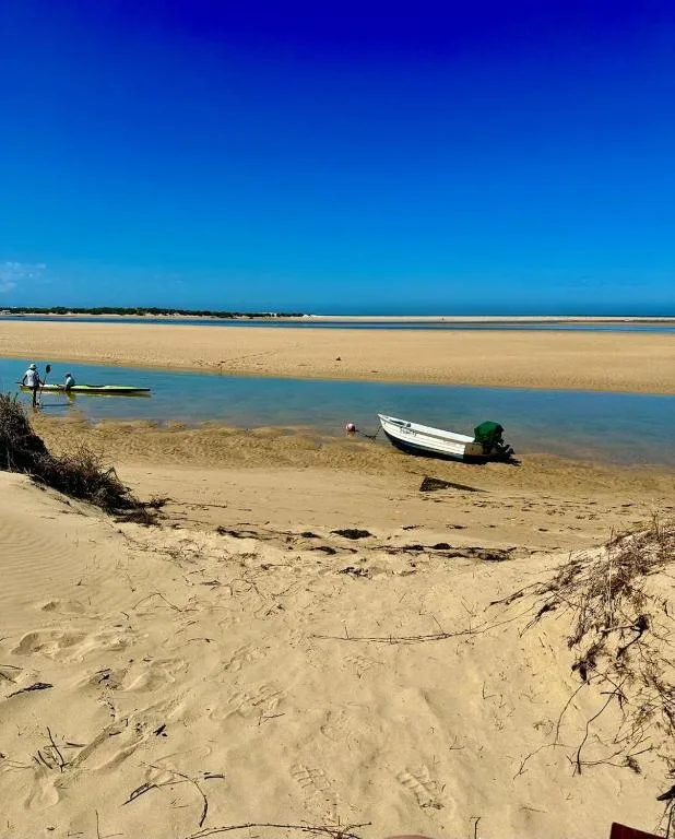 Sandy beach with moored boats and calm lagoon waters, clear blue sky