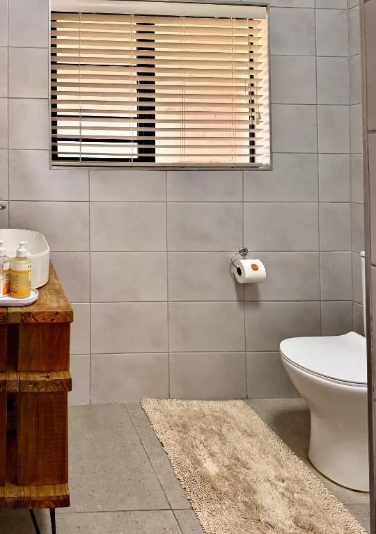 Bathroom with toilet, wooden vanity, tiled walls, and window blinds