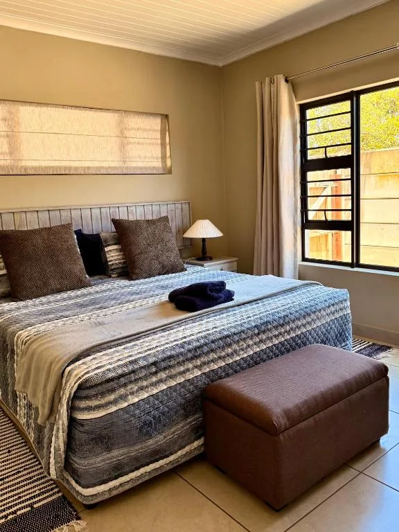 Sunlit bedroom with queen bed, patterned bedding, and garden view