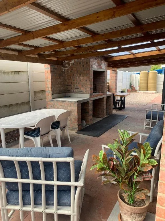 Covered outdoor patio with brick braai, seating, and potted plants