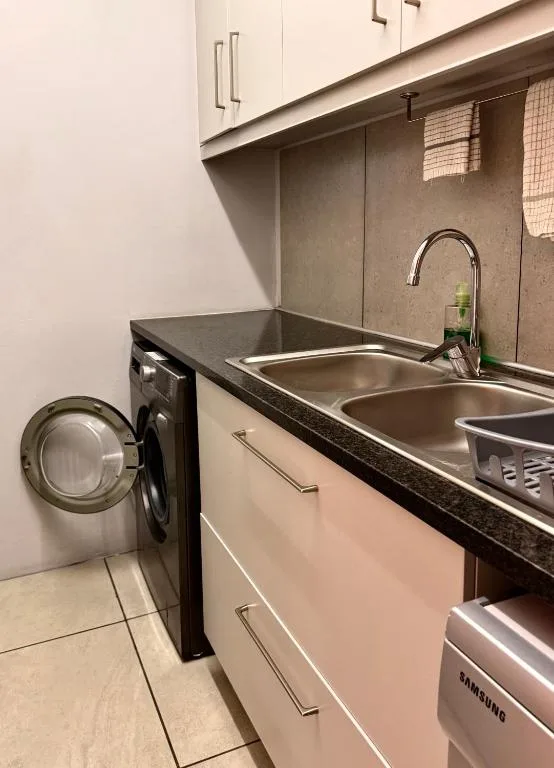 Modern kitchen with double sink, tap, washing machine, and dark countertop