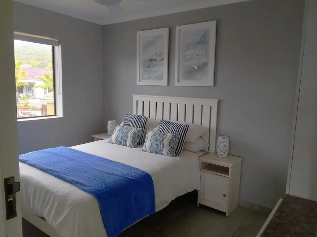 Bright bedroom with double bed, striped pillows, nautical wall art, and garden view