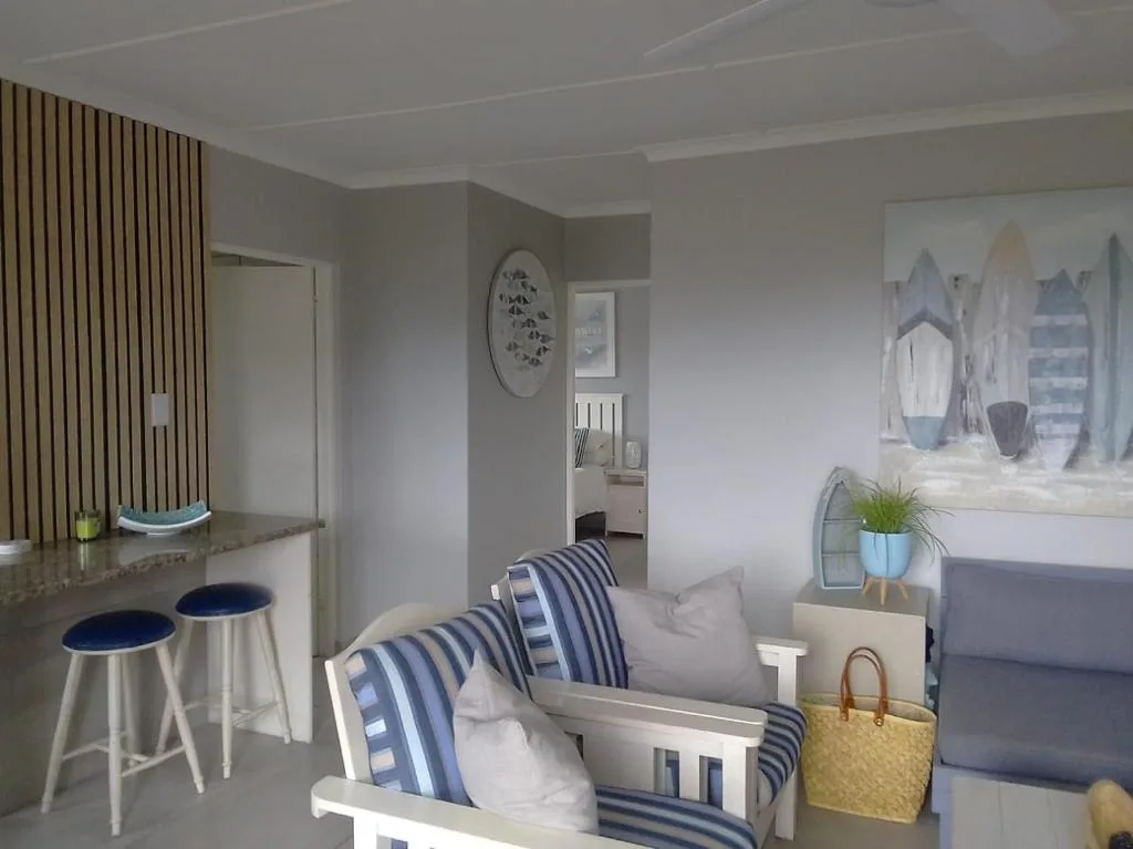 Open-plan lounge with coastal décor, striped cushions, and kitchenette area