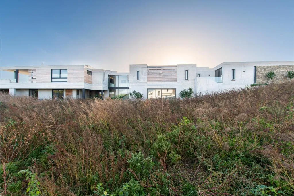 Modern white residential building with coastal vegetation and shrubland in foreground
