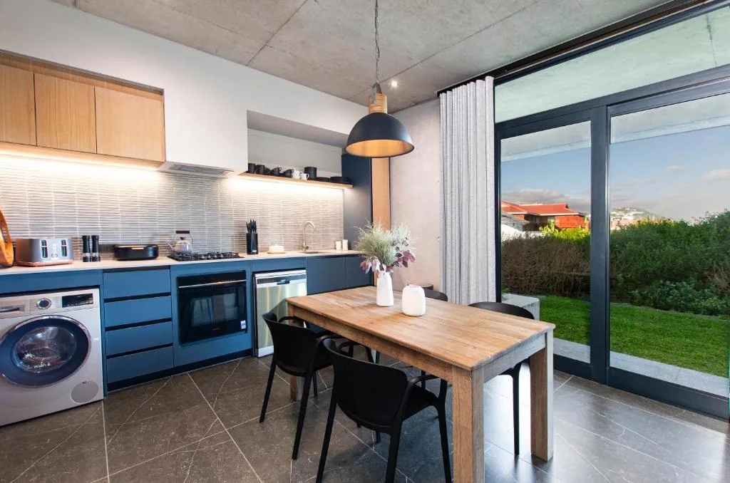 Modern kitchen with blue cabinetry, dining table, and garden view through large sliding doors