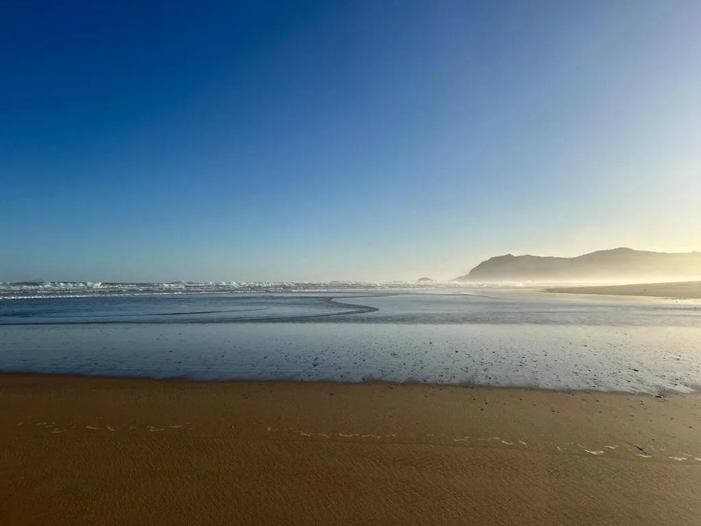Wide sandy beach with gentle waves and misty mountains at sunrise