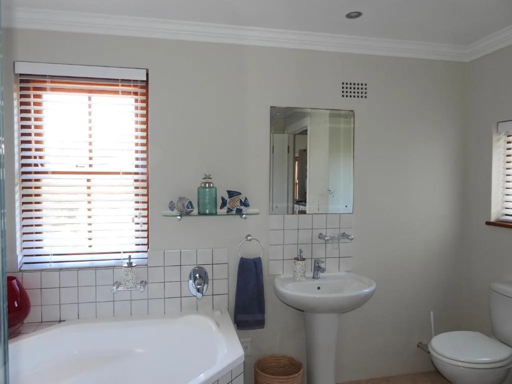 Bright bathroom with white tile walls, pedestal sink, and tub with window