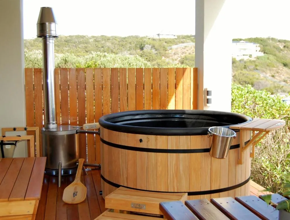 Wooden hot tub with chimney on deck overlooking natural landscape