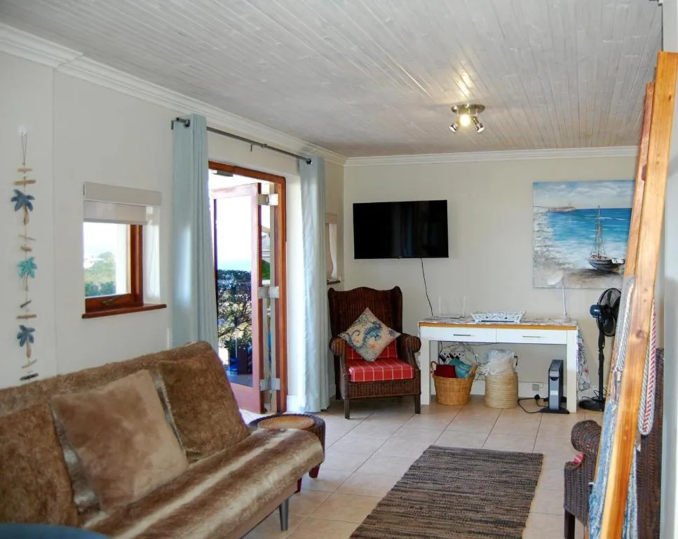 Bright living room with sofa, TV, armchair, and ocean view through glass doors