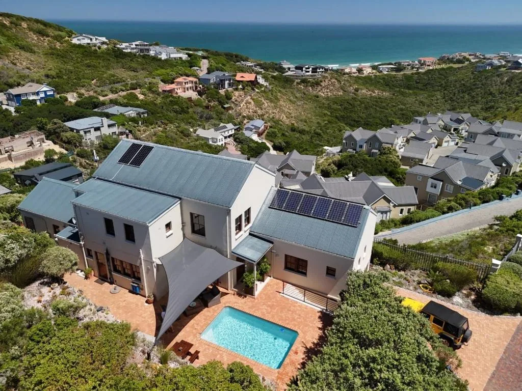 Aerial view of modern home with pool overlooking turquoise ocean and coastal landscape