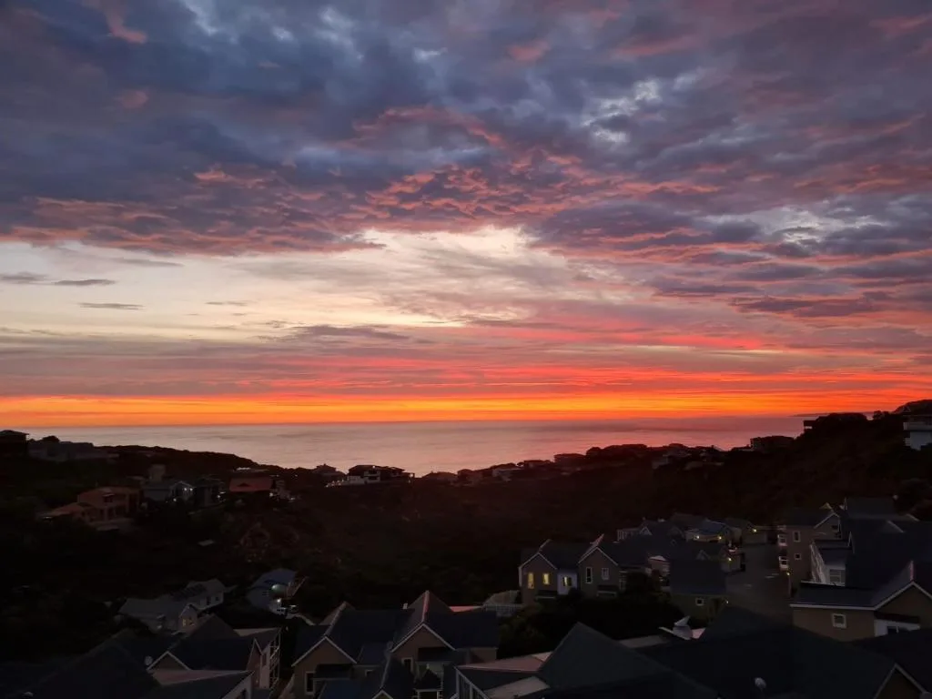 Dramatic sunset over the ocean with silhouetted coastal homes below