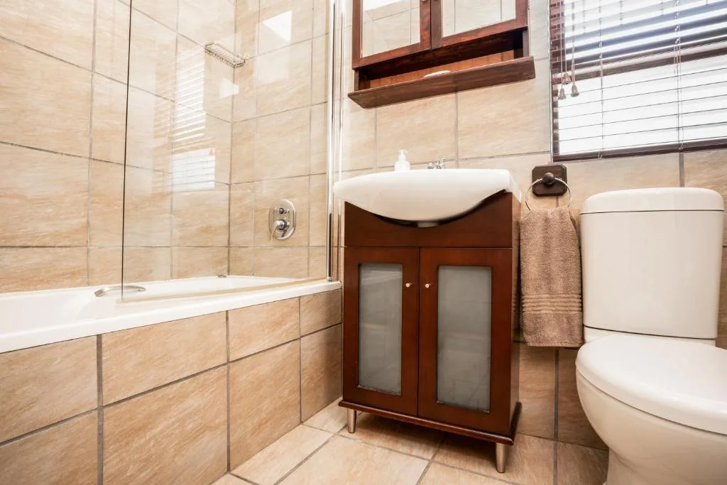 Modern bathroom with beige tile, vanity sink, toilet, and glass shower enclosure
