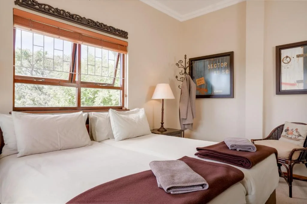 Bright bedroom with white bedding, wooden window frame overlooking green garden views