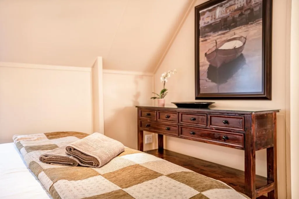 Warm bedroom with quilted bed, wooden dresser, and framed boat artwork