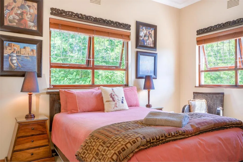 Bright bedroom with twin beds in pink linens and garden views through large windows