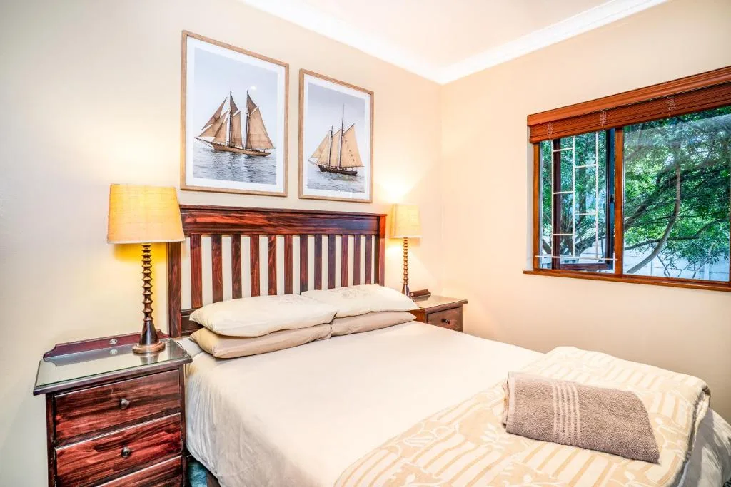 Bright bedroom with wooden bed, sailboat artwork, and garden views
