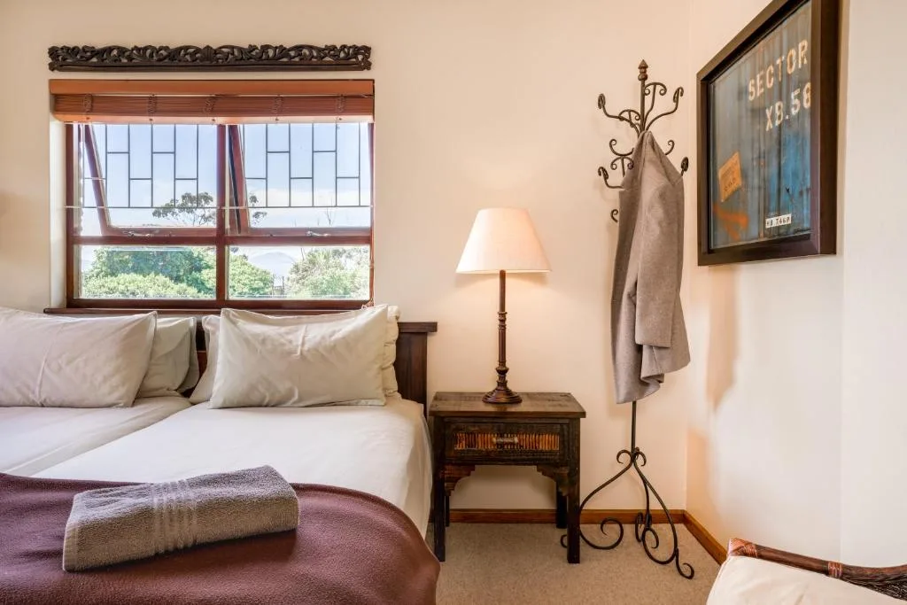 Bright bedroom with white bedding, wooden nightstand, and large windows overlooking gardens